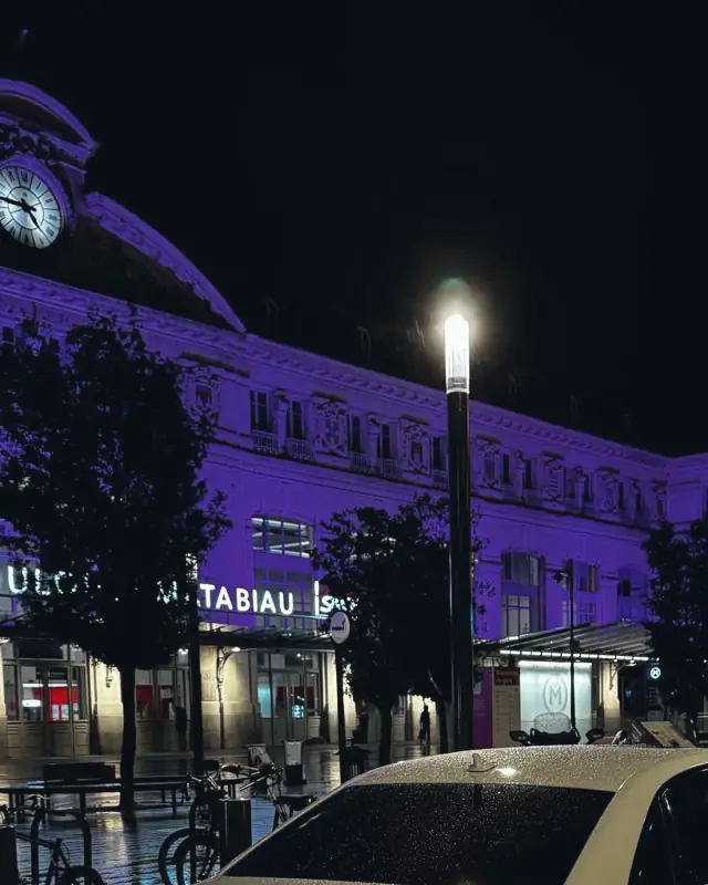 La façade de la gare Toulouse-Matabiau éclairée la nuit, son horloge et son enseigne, le parvis mouillé par la pluie.