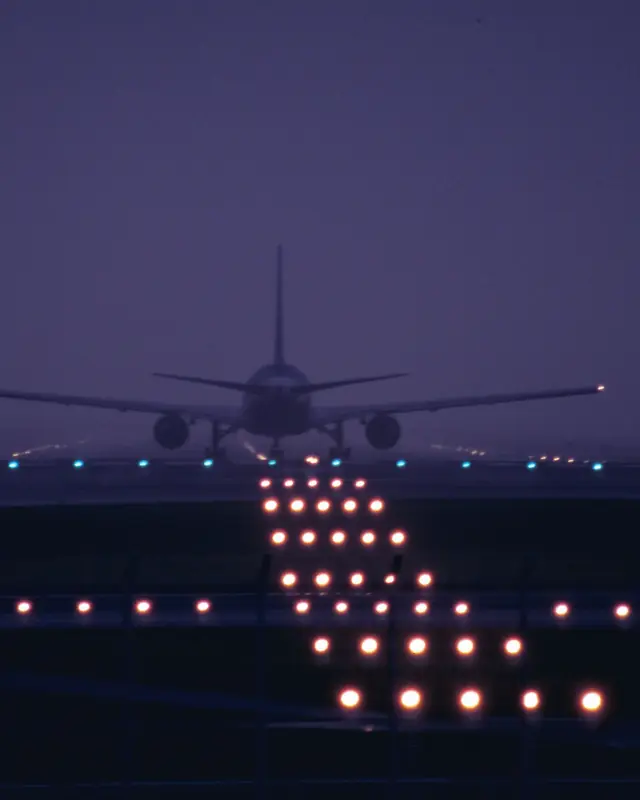 An airliner seen from behind on the runway at the blue hour, the runway lights on ahead of it.
