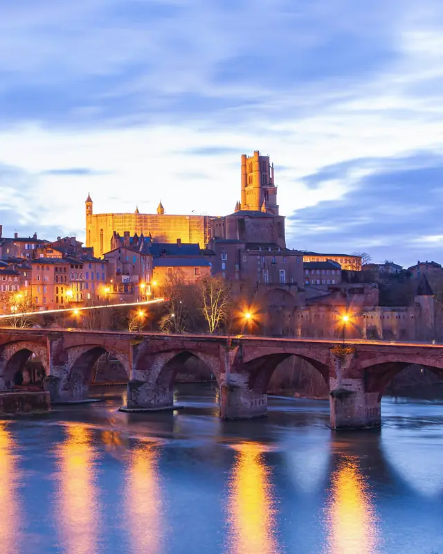 Albi au crépuscule : la cathédrale Sainte-Cécile domine la vieille ville éclairée, le Pont-Vieux et ses lumières dans le Tarn.