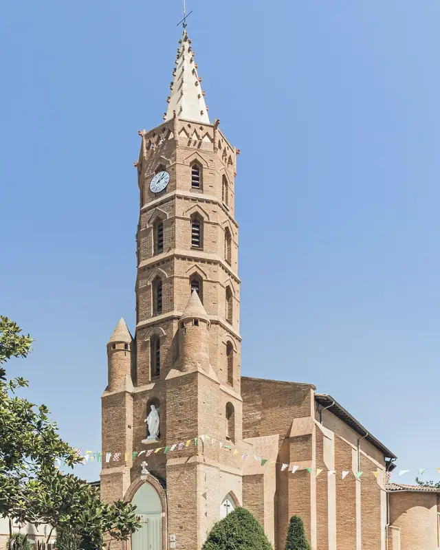 The Church of Saint-Pierre in Blagnac, its tiered brick bell tower and spire, under a blue sky.