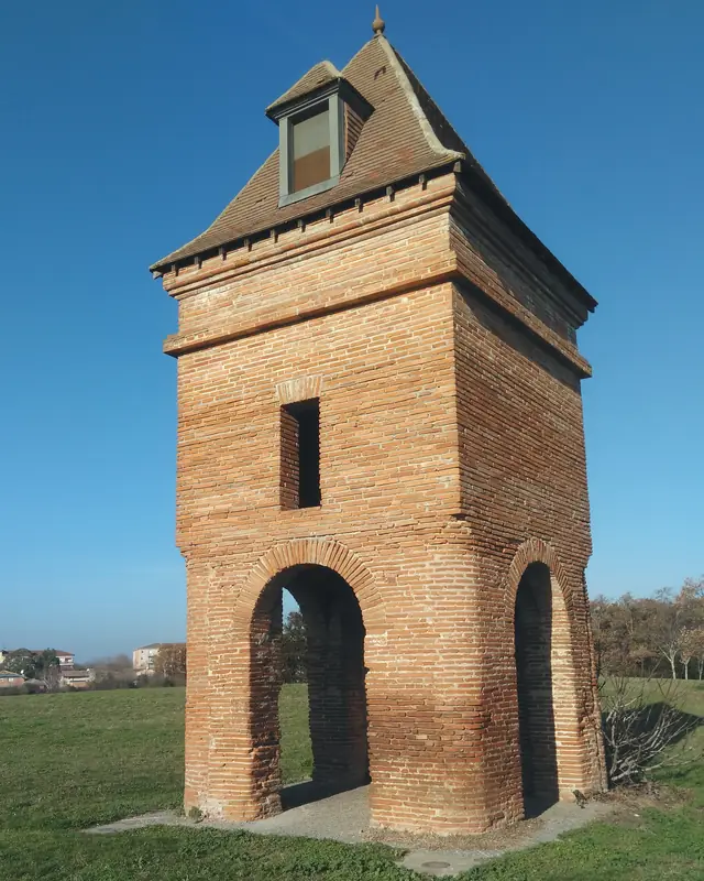 Le pigeonnier du Perget à Colomiers : une tour de brique du XVIIIe siècle posée sur des arcades, son toit de tuiles et sa lucarne, dans un pré.